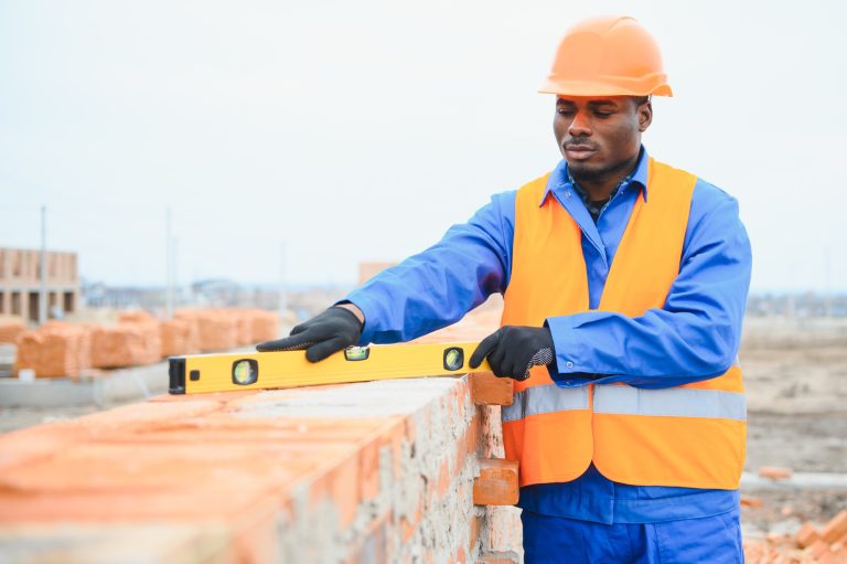 Builder in workwear and protective helmet keeping level handtool on surgace of brick layer